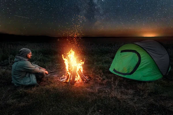 Camping człowiek siedzi przy ognisku w nocy na tle gwiaździstego nieba. Koncepcja podróży, turystyki, kempingu. — Zdjęcie stockowe