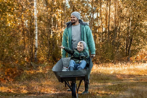 Táta tráví čas se svým synem, šťastným chlapcem, kterého do něj strčil táta. Aktivní venkovní hry pro děti na podzim. — Stock fotografie