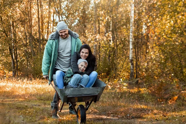 Rodina tráví čas spolu v přírodě, otec válí svého syna a ženu na kolečkách. Aktivní venkovní hry na podzim. — Stock fotografie