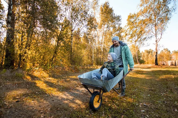 Tata spędza czas ze swoim synem, szczęśliwym chłopcem popychanym przez ojca. Aktywne gry na świeżym powietrzu dla dzieci jesienią. — Zdjęcie stockowe