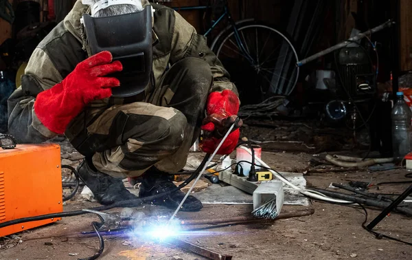 A male welder in a welding mask works with an arc electrode in his garage. Welding, construction, metal work.