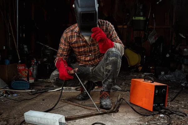 Samec svářeče ve svařovací masce pracuje s obloukovou elektrodou ve své garáži. Svařování, konstrukce, kovoobrábění. — Stock fotografie