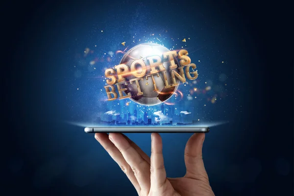 Smartphone en la mano una inscripción dorada Apuestas deportivas con una pelota de fútbol 3D sobre un fondo azul. Apuestas, apuestas deportivas, casa de apuestas. Medios mixtos — Foto de Stock