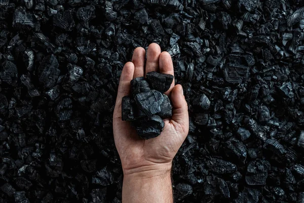 Мужская рука с углем на фоне кучи угля, добыча угля в карьере, копировальная площадка. Ископаемые виды топлива, загрязнение окружающей среды . — стоковое фото