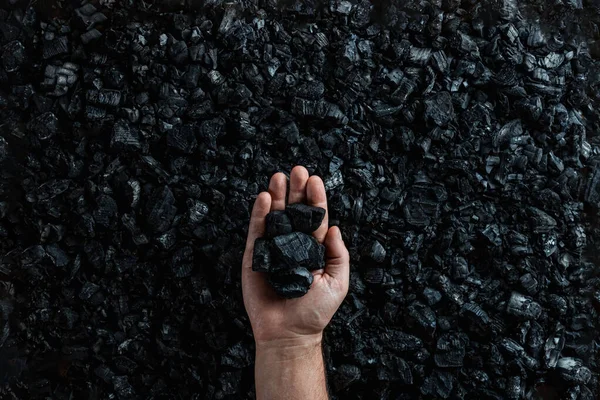 Male hand with coal on the background of a heap of coal, coal mining in an open pit quarry, copy space. Fossil fuels, environmental pollution. — Stock Photo, Image