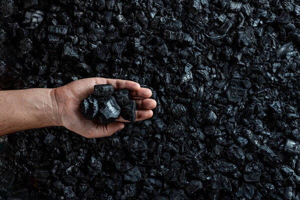 Male hand with coal on the background of a heap of coal, coal mining in an open pit quarry, copy space. Fossil fuels, environmental pollution.