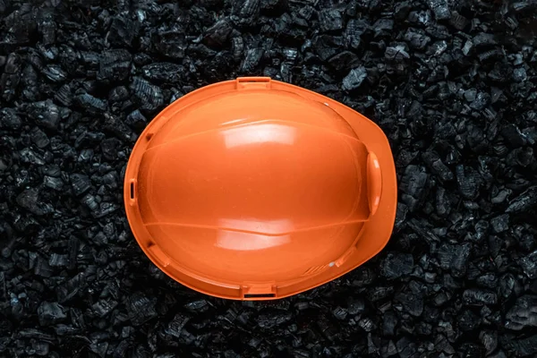 Помаранчевий шолом шахтаря лежить на купі вугілля, відкритого видобутку вугілля, копіювання простору. Вирощування палива, забруднення навколишнього середовища . — стокове фото
