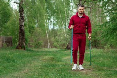 Eşofmanlı bir adam İskandinav yürüyüşü yapıyor. Sağlıklı yaşam tarzı konsepti, kardiyo eğitimi. Kopyalama alanı