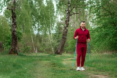 Eşofmanlı bir adam İskandinav yürüyüşü yapıyor. Sağlıklı yaşam tarzı konsepti, kardiyo eğitimi. Kopyalama alanı