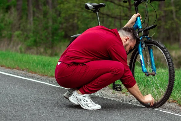 トラックスーツの男が自転車を修理している 自転車修理の概念は 心臓訓練 コピースペース — ストック写真