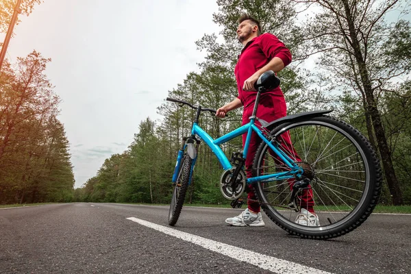 トラックスーツの男は森の中の道路上の自転車の隣に立っている 健康的なライフスタイル 心臓トレーニングの概念 コピースペース — ストック写真