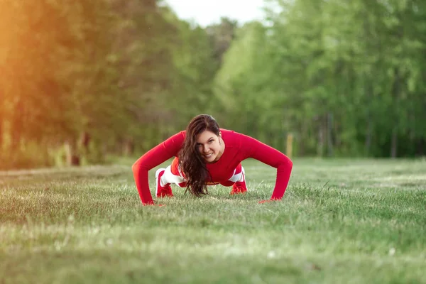 A girl in a sports suit does push-ups, physical exercises on a background of nature. The concept of a healthy lifestyle, exercise, fresh air. Copy space