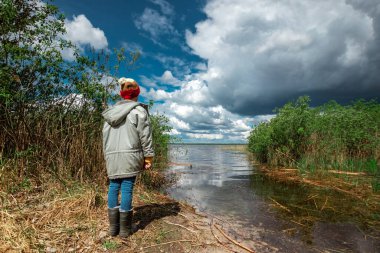 Arka plandaki şapkalı bir çocuk yaz gölünün arka planına karşı