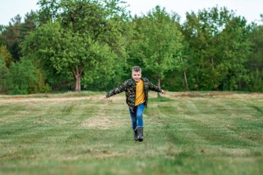 Kollarını yeşilliğin arka planına uzatmış bir çocuk tarlada koşuyor. Hayallerin konsepti, meslek seçimi, pilot, çocukluk. Boşluğu kopyala