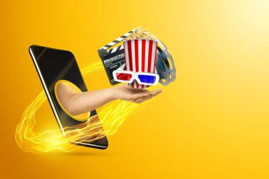 Patlamış mısırlı 3D gözlüklü bir el ve sarı arka plandaki akıllı telefon ekranına yayılmış bir wilm board. Çevrimiçi sinema kavramı, telefondaki yayın platformları, modern teknolojiler..