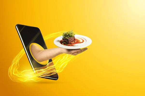 Hand serves a restaurant dish via smartphone on a yellow background. The concept of food delivery, online ordering, restaurant services at home