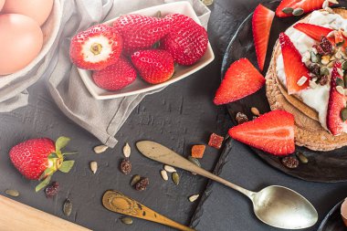 Birkaç çilek rustik koyu arka plan üzerinde bir tabakta. Çeşitli malzemeler ve nesneleri, çatal, kaşık, peçete.