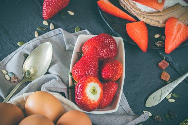 Birkaç çilek rustik koyu arka plan üzerinde bir tabakta. Çeşitli malzemeler ve nesneleri, çatal, kaşık, peçete.