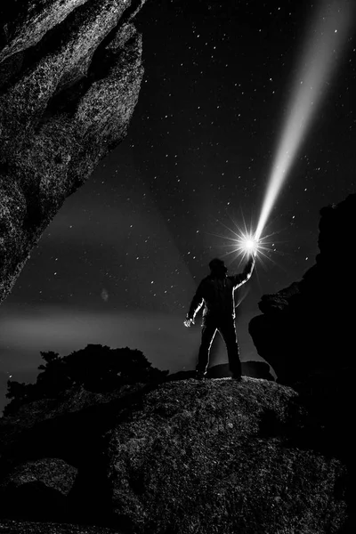 岩石上的人用非常强大的手电筒照亮了黑暗的夜空 — 图库照片