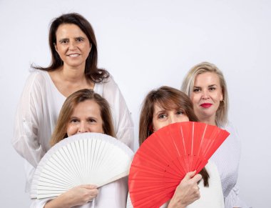 4 kadın, arkadaş, orta yaşlı beyaz arka plan ile bir stüdyoda fotoğraf oturumunda eğleniyor, bir top üzerinde oturan ve bir yelpaze ile oynayan Grup
