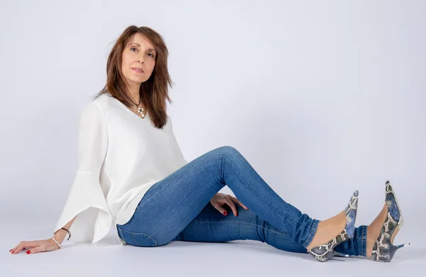 Photographic studio session for a 50 year old woman sitting on the floor and dressed in jeans and white shirt.