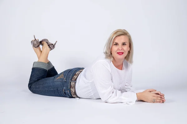 Photographic studio session for a 50 year old woman sitting on the floor and dressed in jeans and white shirt.