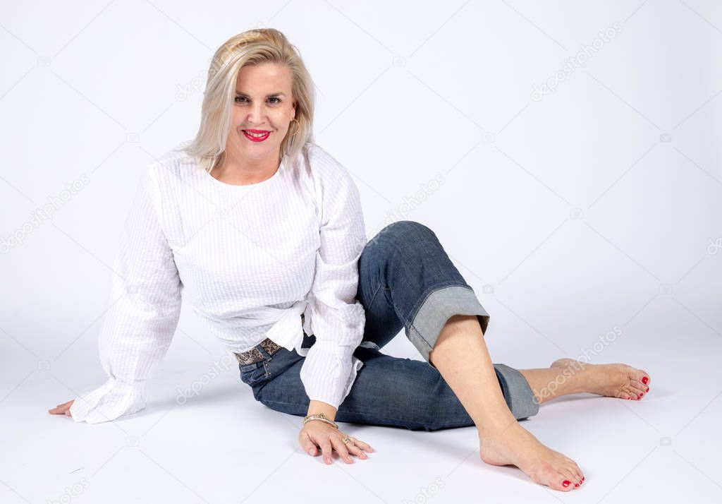 Photographic studio session for a 50 year old woman sitting on the floor and dressed in jeans and white shirt.