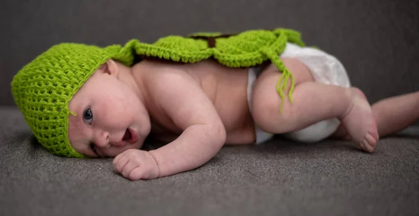 Bambino di tre mesi sdraiato su un divano e travestito da tartaruga verde . — Foto Stock