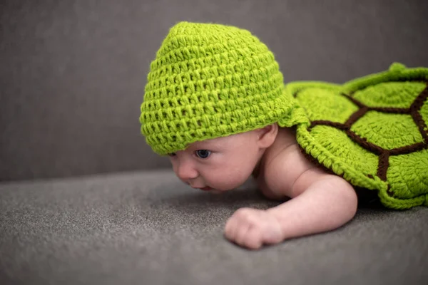 Bambino di tre mesi sdraiato su un divano e travestito da tartaruga verde . — Foto Stock