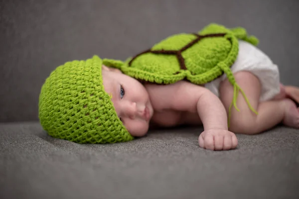 Three-month-old baby lying on a sofa and disguised as a green turtle. — Stock Photo, Image