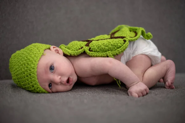 Bambino di tre mesi sdraiato su un divano e travestito da tartaruga verde . — Foto Stock
