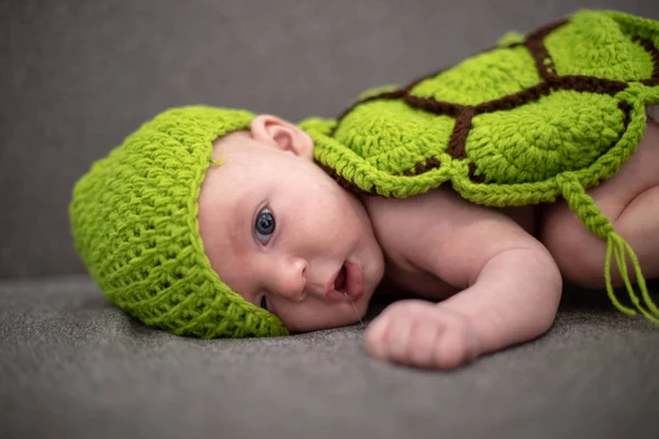 Bambino di tre mesi sdraiato su un divano e travestito da tartaruga verde . — Foto Stock