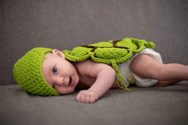 three-month-old baby lying on a sofa and disguised as a green turtle.