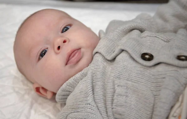 Bambino sdraiato con un maglione grigio guarda attentamente — Foto Stock