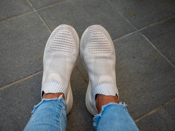 Feet of a woman wearing white designer shoes and light blue jeans. — Stock Photo, Image