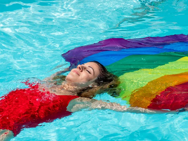 Kaukasische blonde meisje drijft in het zwembad met de vlag van Pride. — Stockfoto