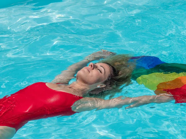 Kaukasische blonde meisje drijft in het zwembad met de vlag van Pride. — Stockfoto