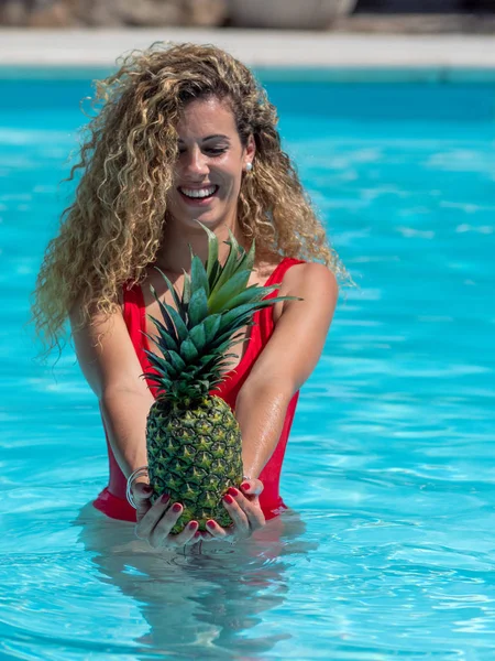 Menina loira branca brinca com um abacaxi na piscina . — Fotografia de Stock