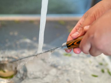 Musluk altında yıkanan adamın elleri mutfak bıçağı.