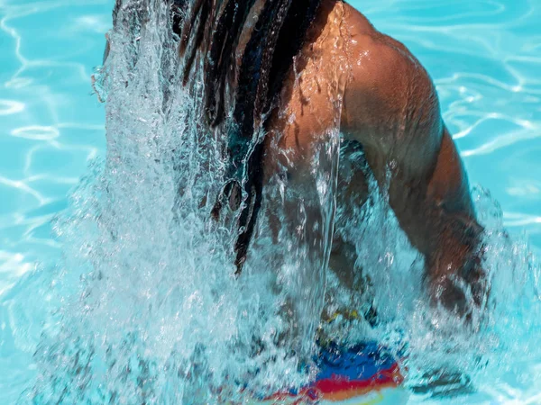 Black man with afro hair and dreadlocks comes out of the pool splashing water.