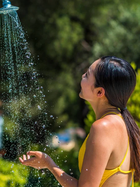 Asian girl in yellow bikini takes a shower by the pool. — Stockfoto