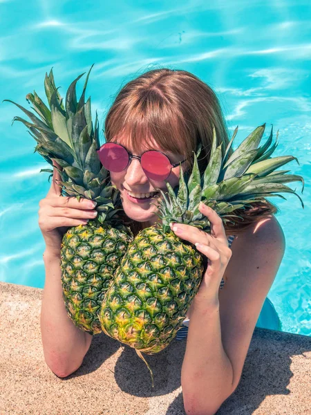 Menina caucasiana ruiva, posa junto à piscina com dois abacaxis . — Fotografia de Stock