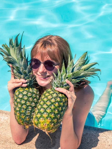 Roodharige Kaukasische meisje, poses bij het zwembad met twee ananassen. — Stockfoto