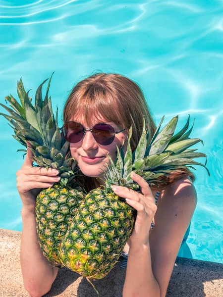 Menina caucasiana ruiva, posa junto à piscina com dois abacaxis . — Fotografia de Stock
