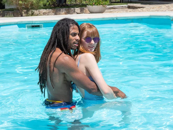 Interracial paar in de liefde, spelen in het zwembad. Het meisje zeer wit en rood haar en de jongen zwart. — Stockfoto