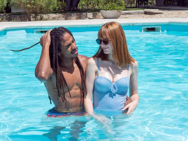 Casal inter-racial apaixonado, jogar na piscina. A menina cabelo muito branco e vermelho e o menino preto . — Fotografia de Stock