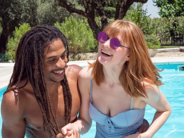 Interracial paar in de liefde, spelen in het zwembad. Het meisje zeer wit en rood haar en de jongen zwart. — Stockfoto