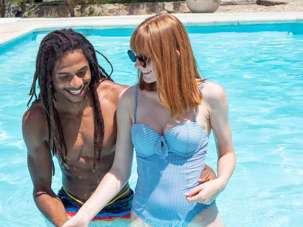 Interracial paar in de liefde, spelen in het zwembad. Het meisje zeer wit en rood haar en de jongen zwart. — Stockfoto
