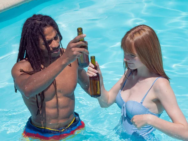 Interracial paar spelen in het zwembad. Ze is op zijn schouders en ze drinken bier — Stockfoto