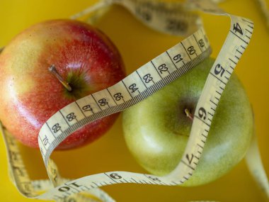 Bodegon sarı bir arka plan üzerine monte edilmiş ve iki elma ve bel ölçmek için bir bant oluşan.